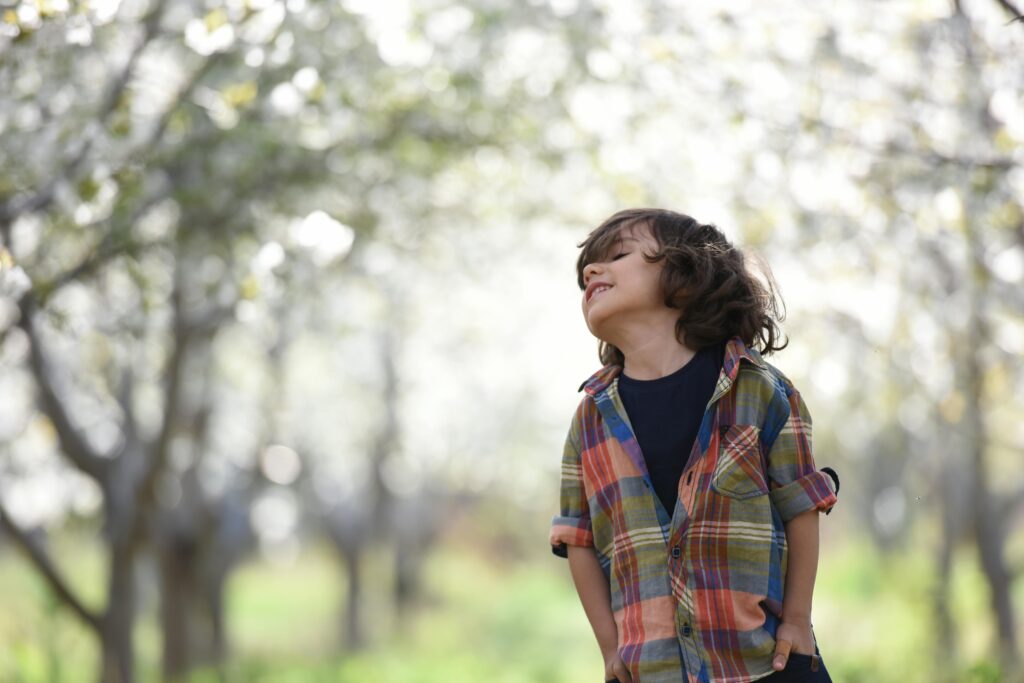 A joyful child in a colorful plaid shirt outdoors, enjoying a spring day.